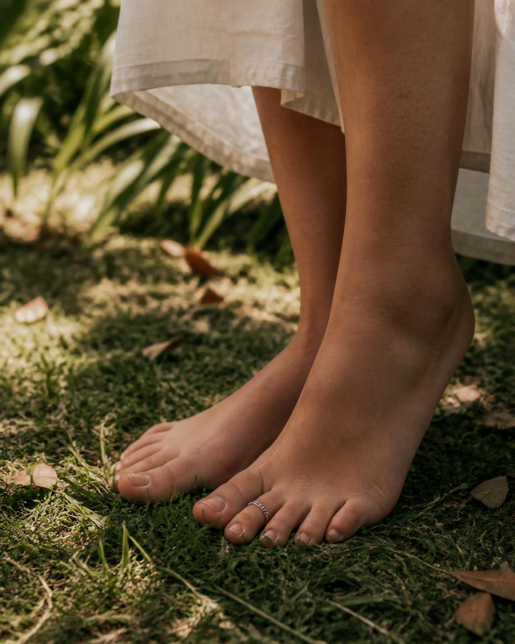 Warm bare feet standing softly on rustic green grass with a small silver toe ring
